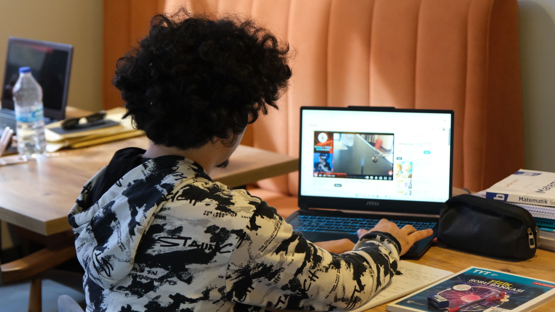 Teenager using a laptop for learning at home, surrounded by study materials and books.