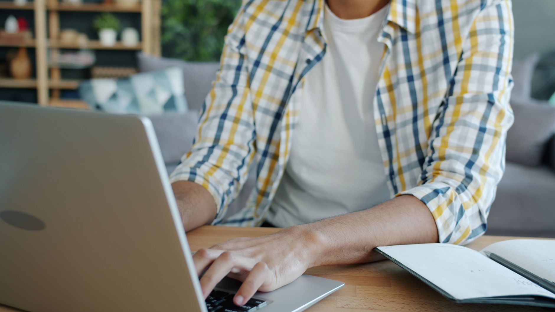 A young adult man typing on a laptop in a comfortable home setting.
